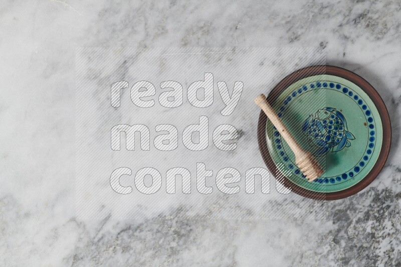 طبق فخاري مزخرف مع ملعقة عسل خشبية بداخله على خلفية من الرخام الرمادي