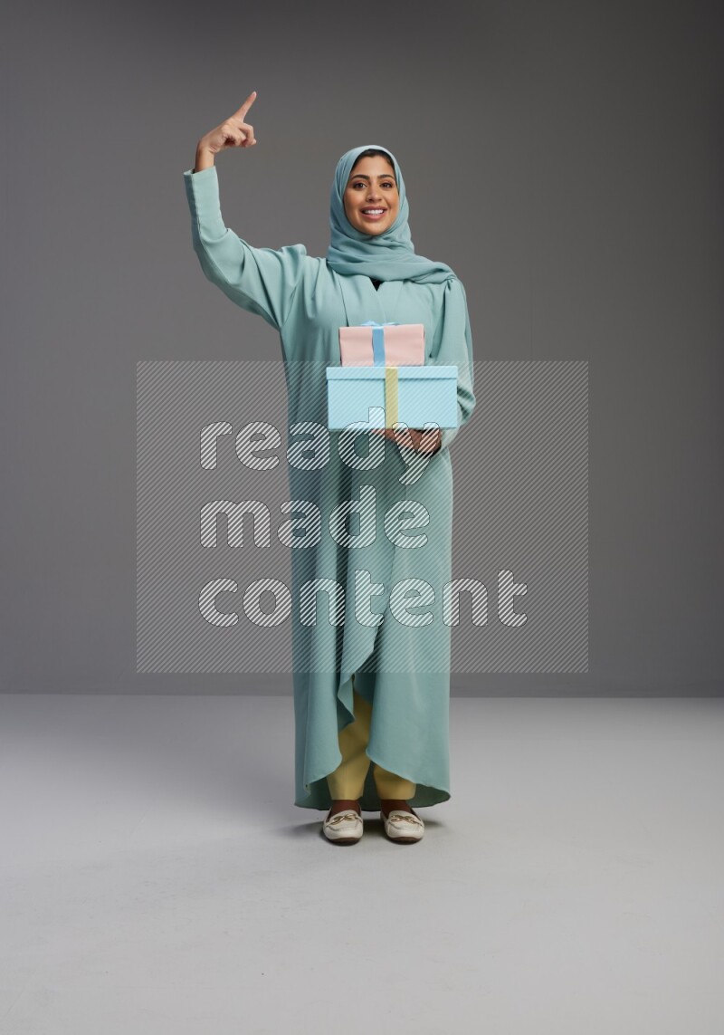 Saudi Woman wearing Abaya standing holding gift box on Gray background