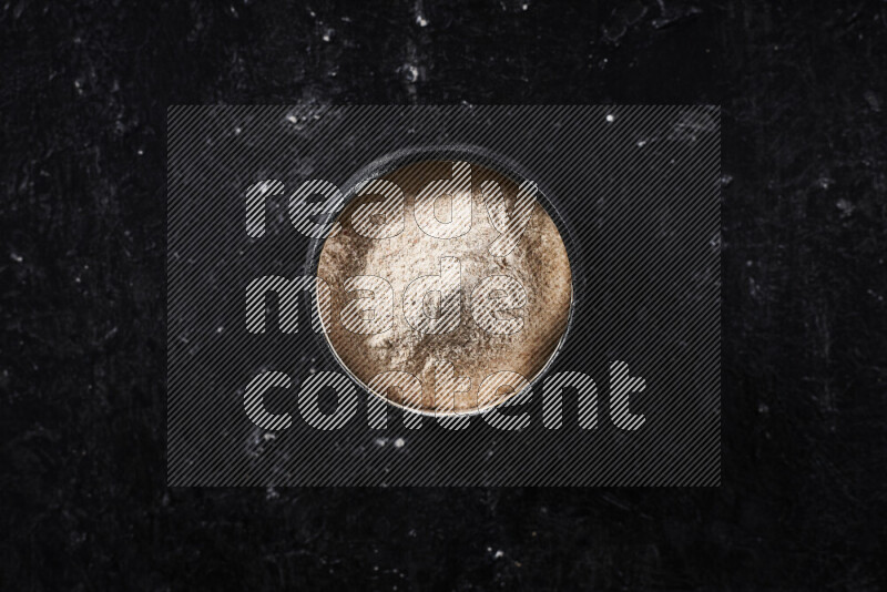 A black pottery bowl full of onion powder on black background
