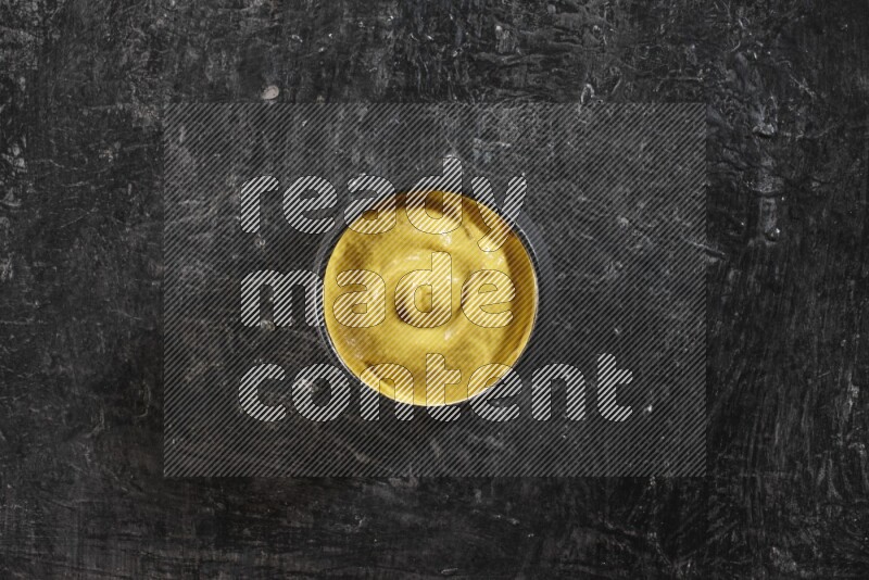 A black pottery bowl full of mustard paste on textured black flooring