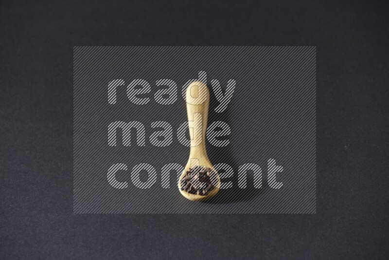 A wooden spoon full of cloves on a black flooring