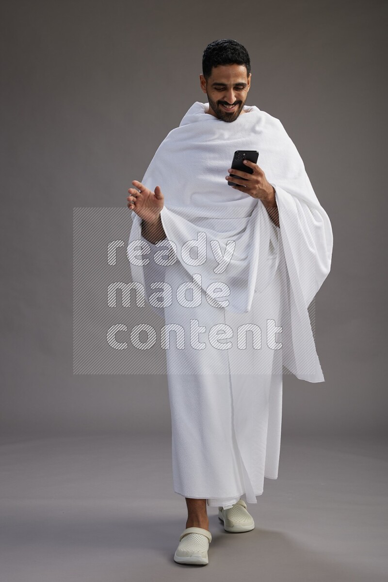 A man wearing Ehram Standing texting on phone on gray background