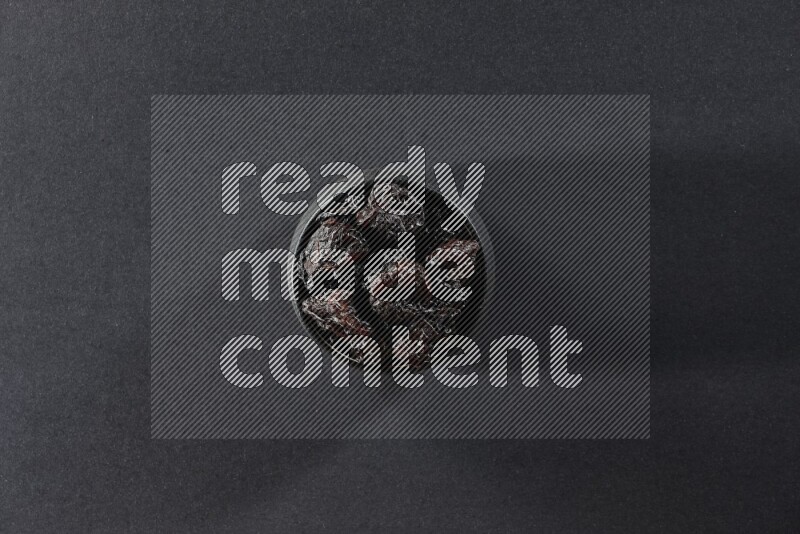 وعاء فخاري أسود ممتلئ بالبرقوق المجفف على خلفية سوداء