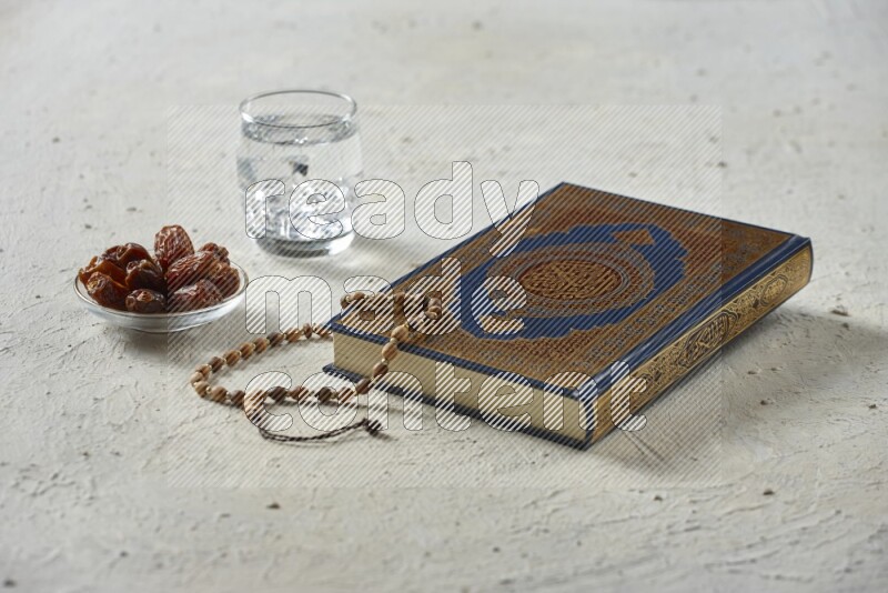 Quran with dates, prayer beads and different drinks all placed on textured white background