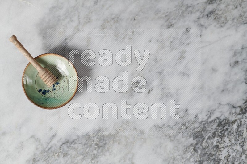 Decorative pottery plate with wooden honey dipper in it on grey marble background