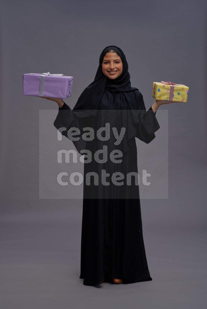 Saudi woman wearing Abaya standing holding gift box on gray background