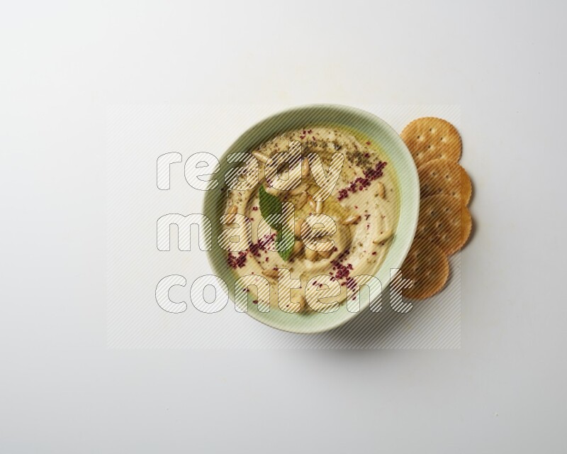 Hummus in a green plate garnished with zattar & sumak on a white background
