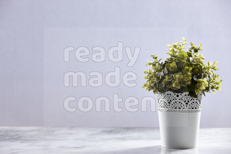 Green artificial plant in white decorative pot on grey marble background