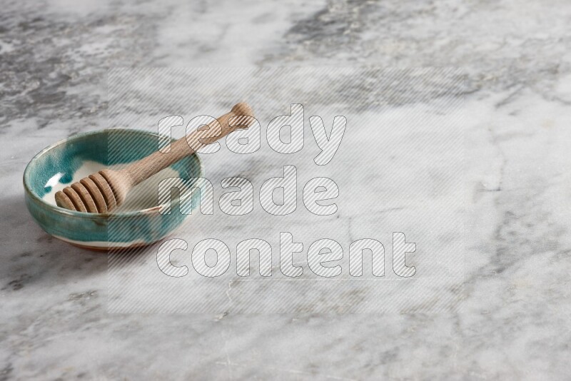 Multicolored pottery bowl with wooden honey dipper in it on grey marble background