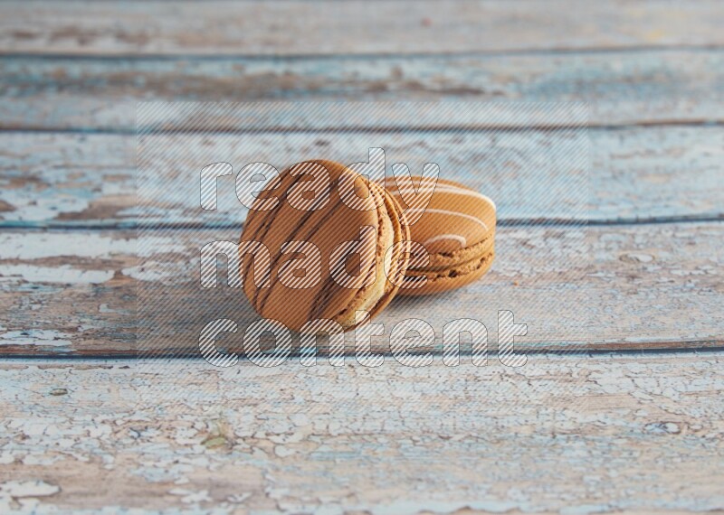 45º Shot of of two assorted Brown Irish Cream, and light brown Almond Cream macarons next to each other on light blue background