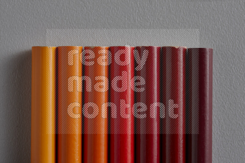 A collection of colored pencils arranged showcasing a gradient of orange and red hues on grey background