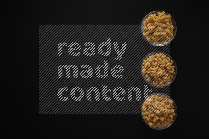 Different pasta types in 3 glass bowls on black background