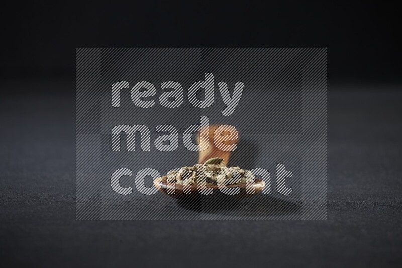 مغرفة خشبية ممتلئة بالهيل على خلفية سوداء