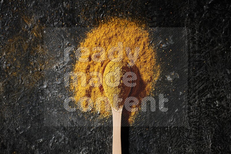 A wooden spoon full of turmeric powder on textured black background