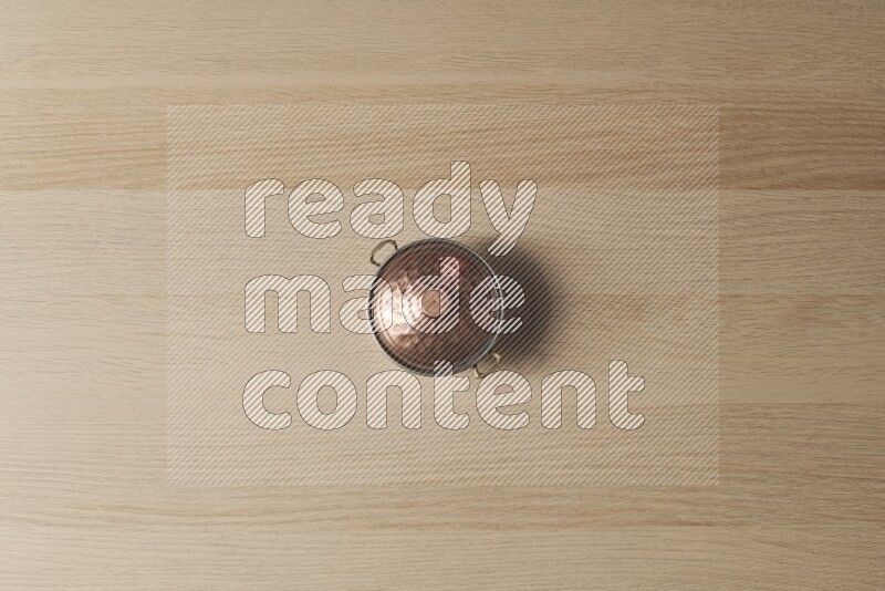 A small copper pot on light wooden background