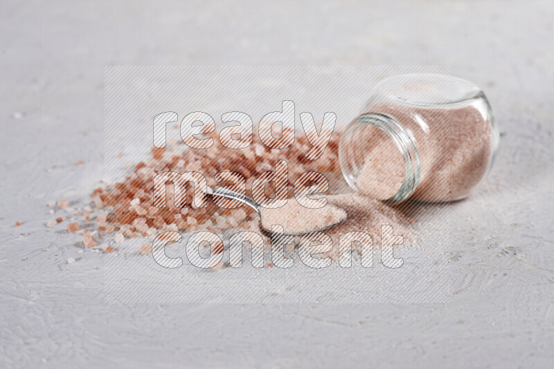 A glass jar full of fine himalayan salt with some himalayan crystals beside it on a white background