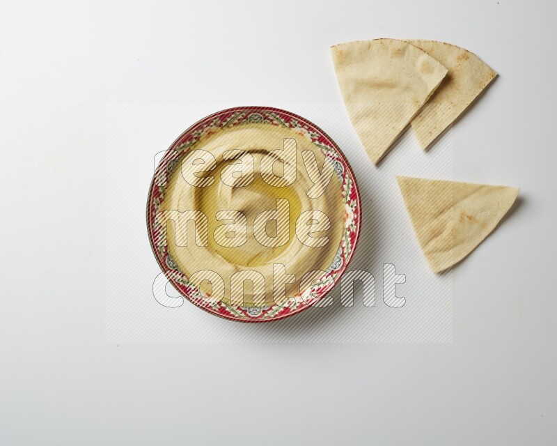 Hummus in a red plate with patterns garnished with olive oil on a white background