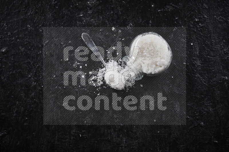 A glass jar full of coarse sea salt crystals on black background