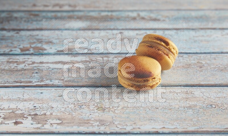 45º Shot of two Yellow Crème Brulée macarons on light blue wooden background
