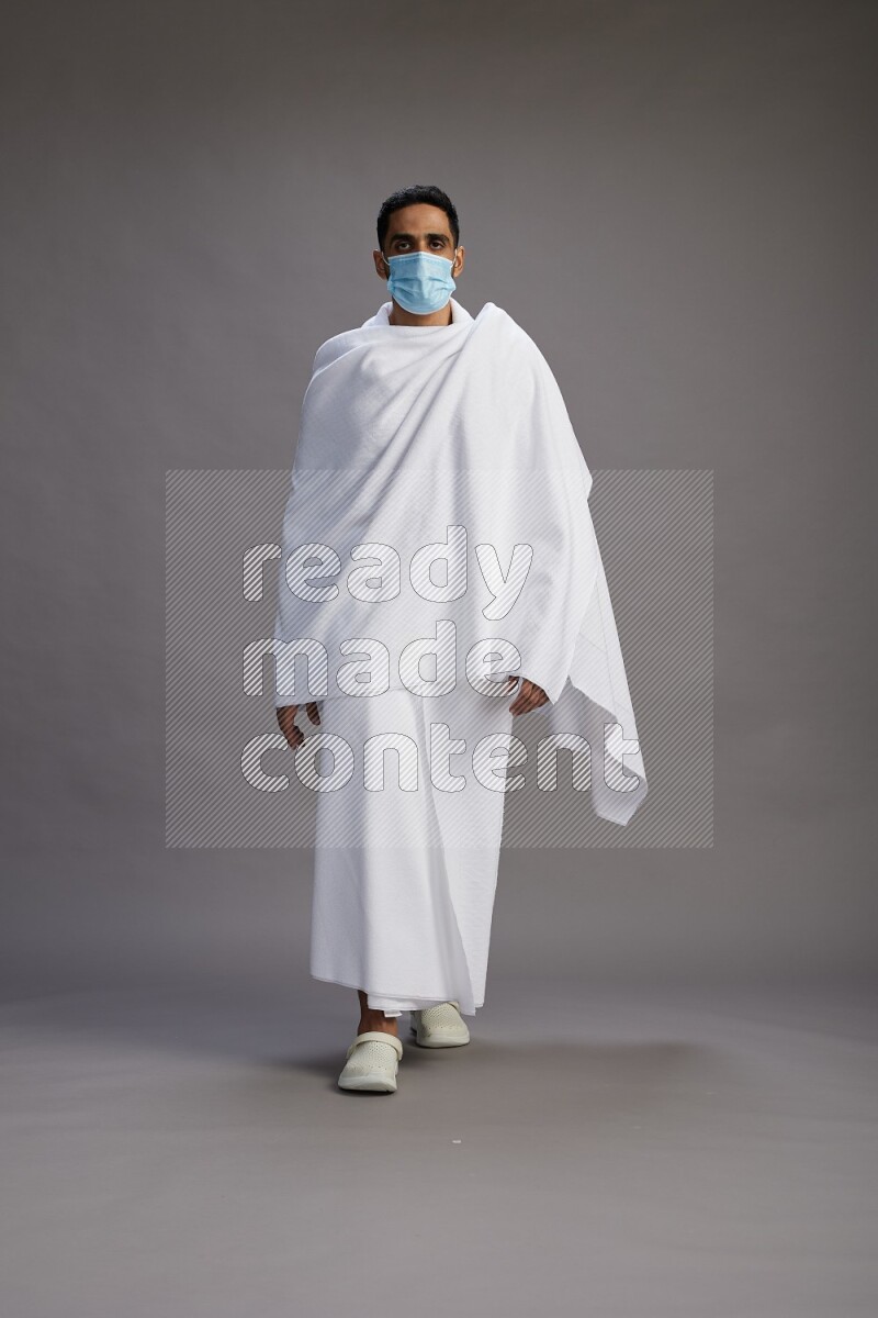 A man wearing Ehram with face mask Standing Interacting with the camera on gray background