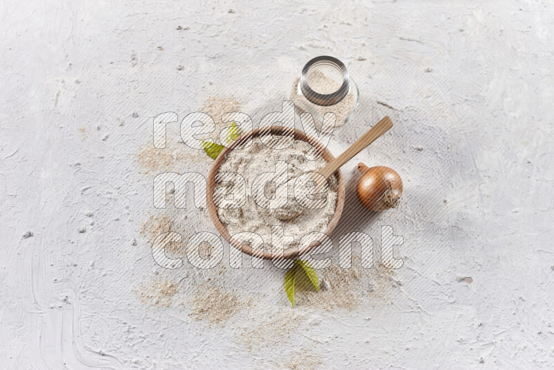 A wooden bowl full of onion powder with a glass jar beside it and fresh onion on white background