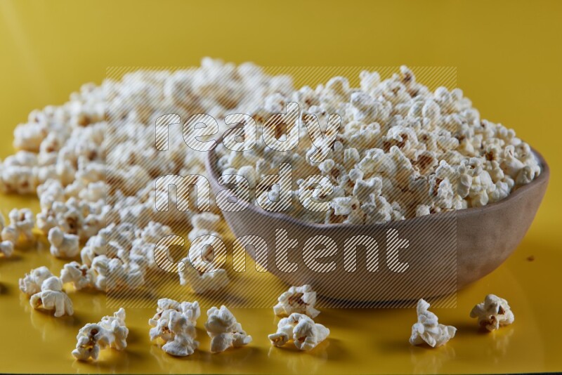 A brown pottery bowl full of popcorn with popcorn beside it on a yellow background in different angles