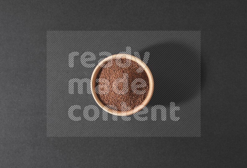 A wooden bowl full of garden cress seeds on a black flooring
