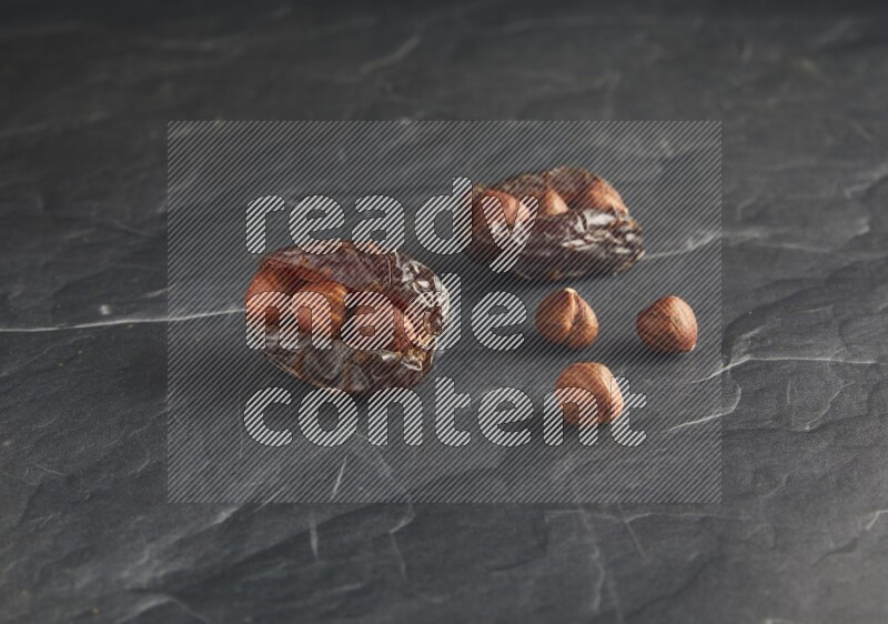 two hazelnuts stuffed madjoul dates on a black textured background
