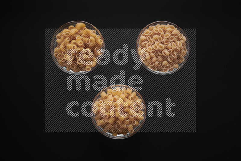 Different pasta types in glass bowls on black background
