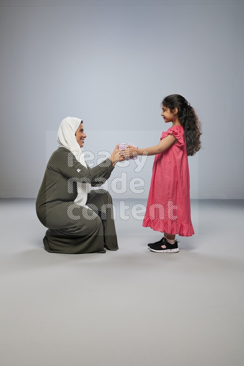 A girl giving a gift to her mother on gray background