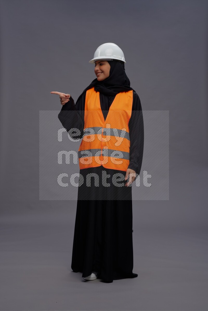 Saudi woman wearing Abaya with engineer vest standing interacting with the camera on gray background