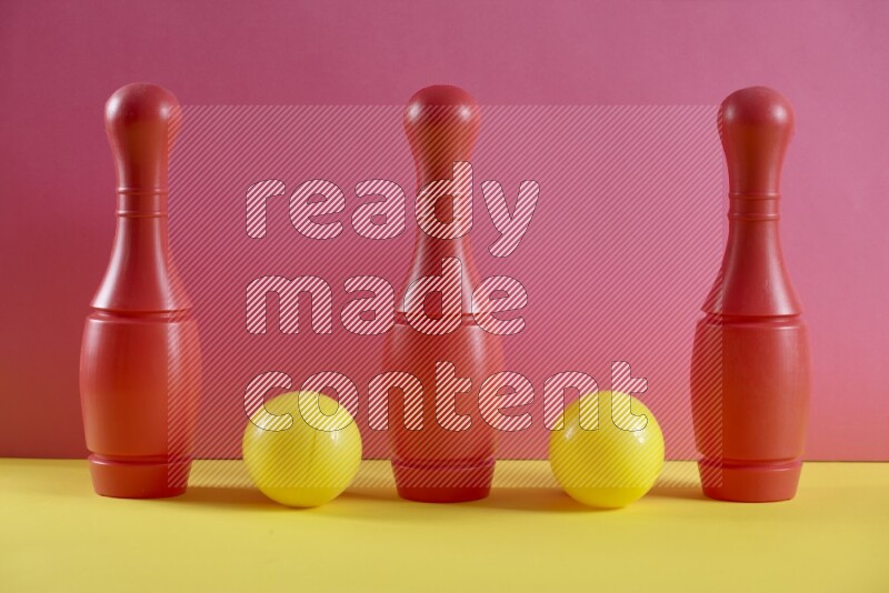 Plastic bowling pins with balls on pink and yellow background (kids toys)