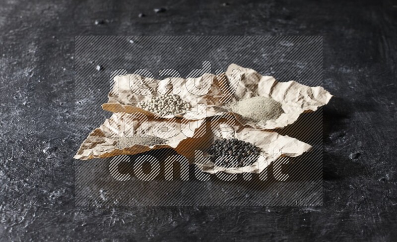 Crumpled pieces of paper full of black and white pepper beads and powder on a textured black flooring