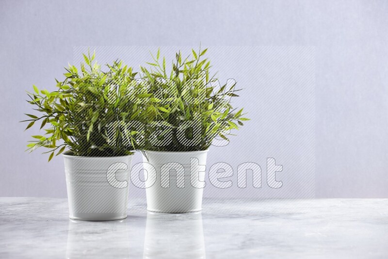 Two green artificial plants in white pot on grey marble background