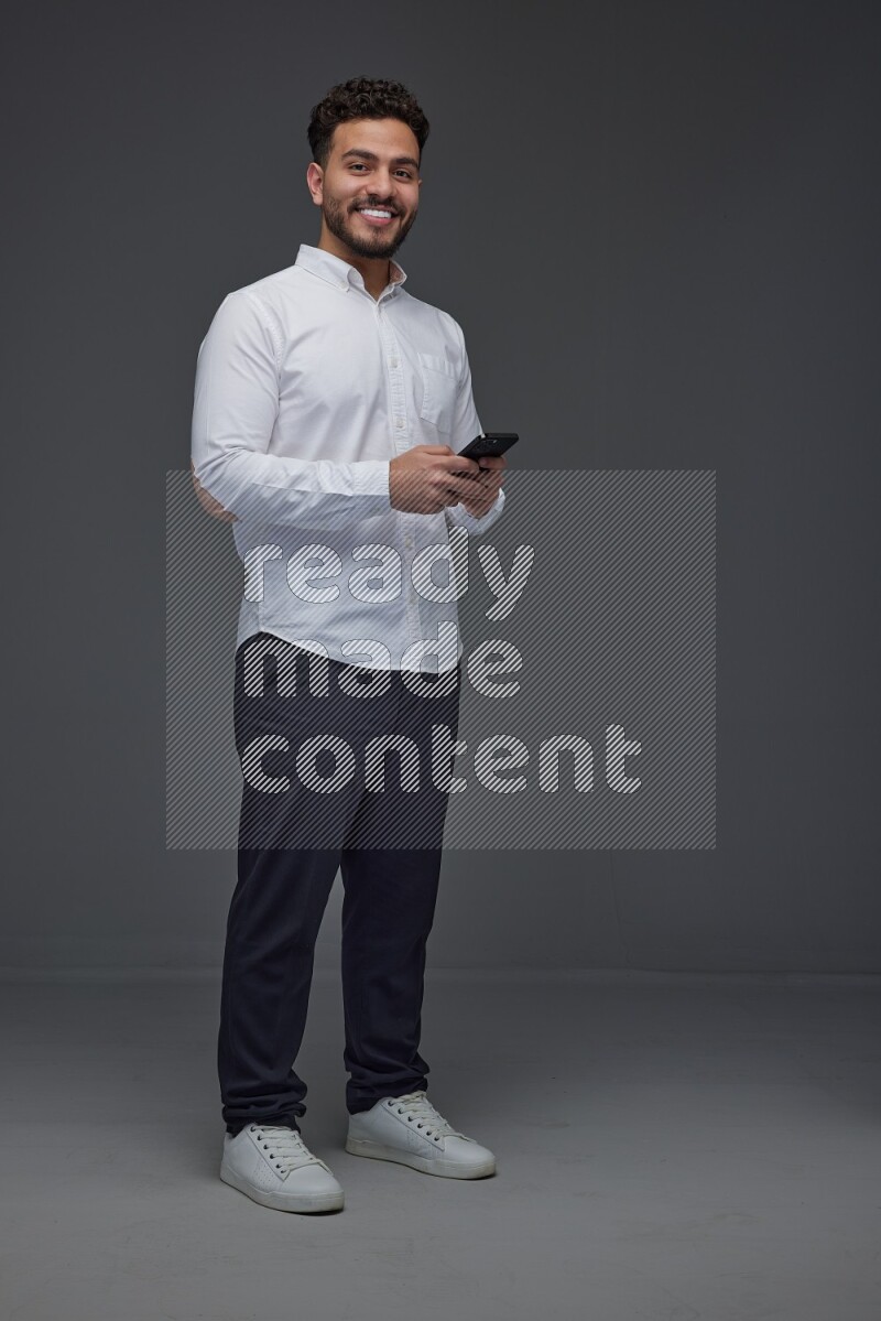 A man wearing smart casual standing and using his phone eye level on a gray background