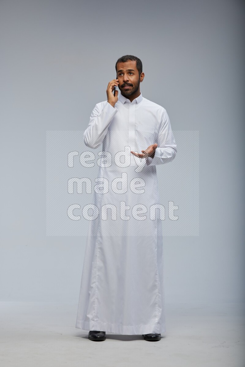 Saudi man wearing Thob standing talking on phone on Gray background