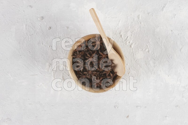 Star anise in a wooden bowl with a wooden spoon in it on white background