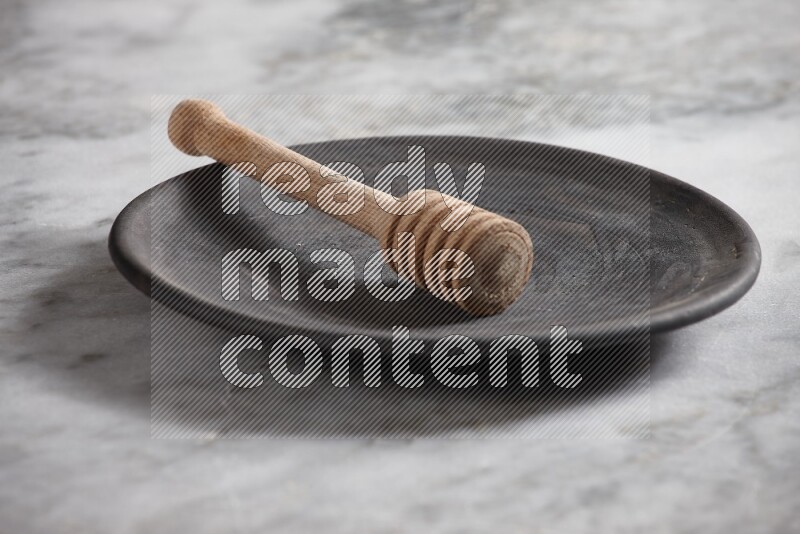 Black pottery plate with wooden honey dipper in it on grey marble background