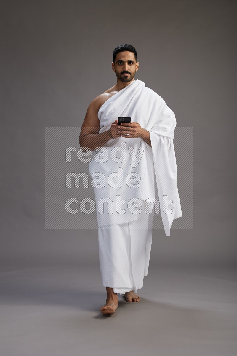 A man wearing Ehram Standing texting on phone on gray background