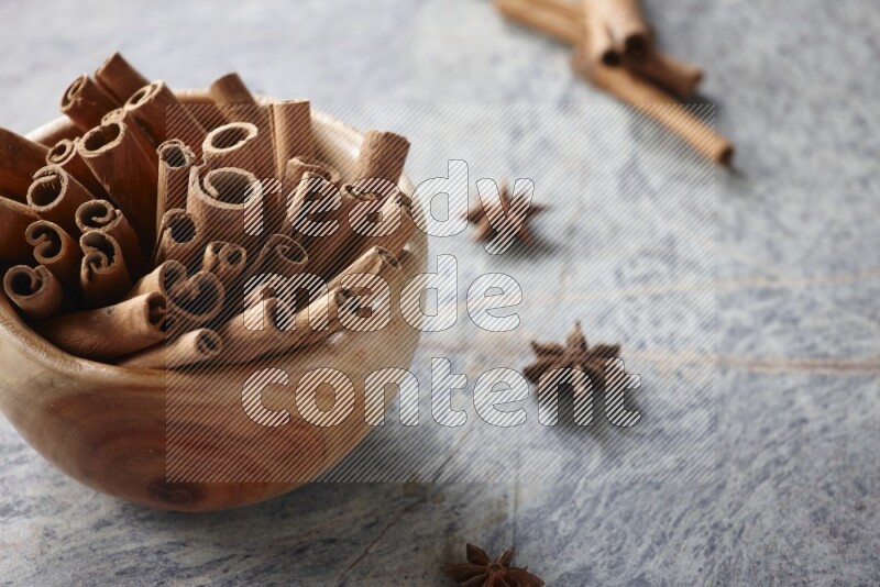 wooden bowl full of cinnamon sticks surrounded by star anis on marble background in different angles