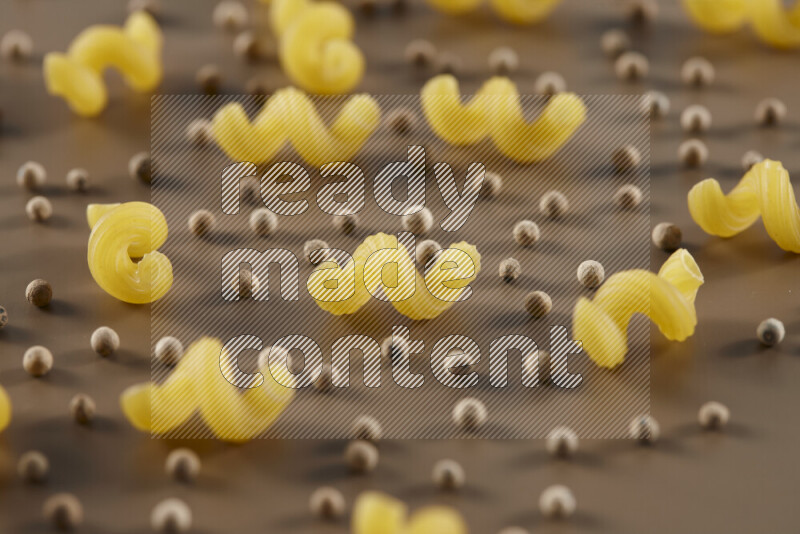 Raw pasta with different ingredients such as cherry tomatoes, garlic, onions, red chilis, black pepper, white pepper, bay laurel leaves, rosemary and cardamom on beige background