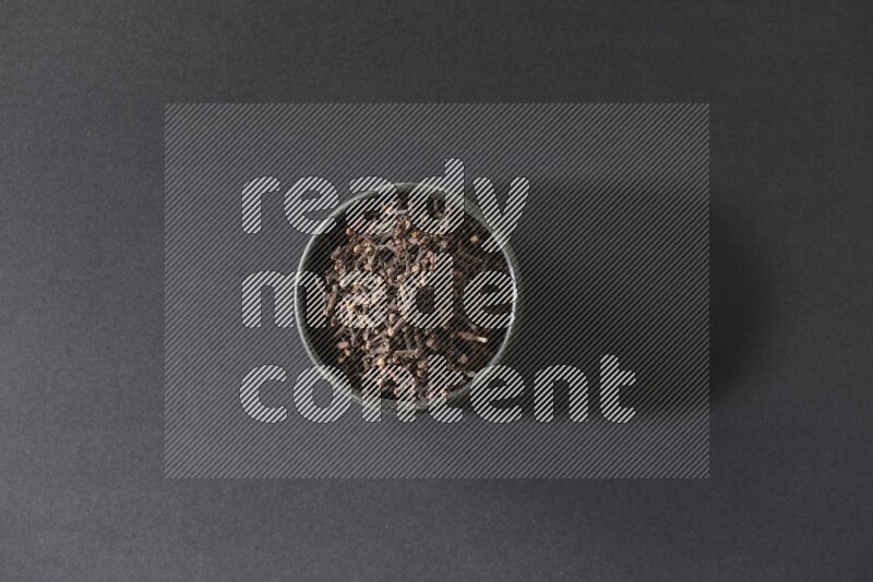 A black pottery bowl full of cloves on a black flooring