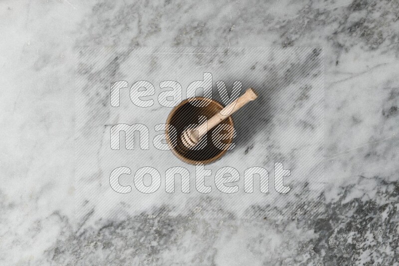 Multicolored pottery bowl with wooden honey dipper in it on grey marble background