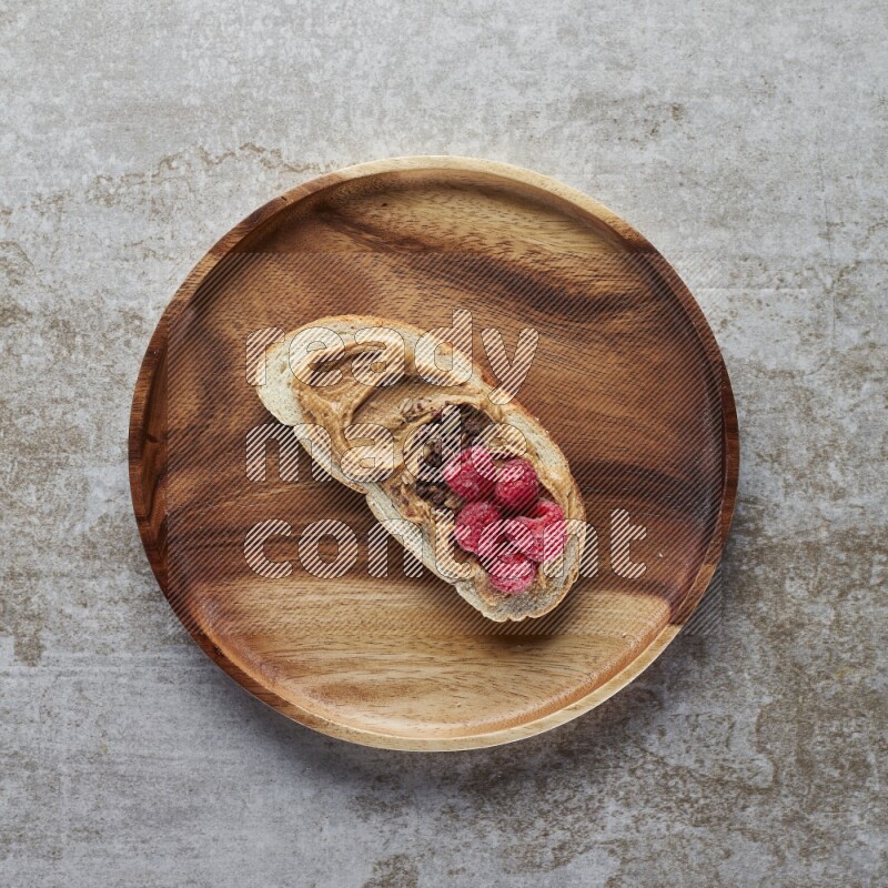 open faced peanut butter sandwich with raspberries and chocolate granula on a grey textured background