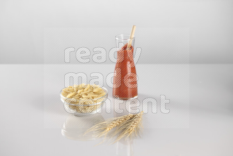 Raw pasta with tomatoe pasta with different ingredients such as cherry tomatoes, basil, garlic, bay laurel, cardamom, white pepper, black pepper, red chilis and wheat stalks on light grey background