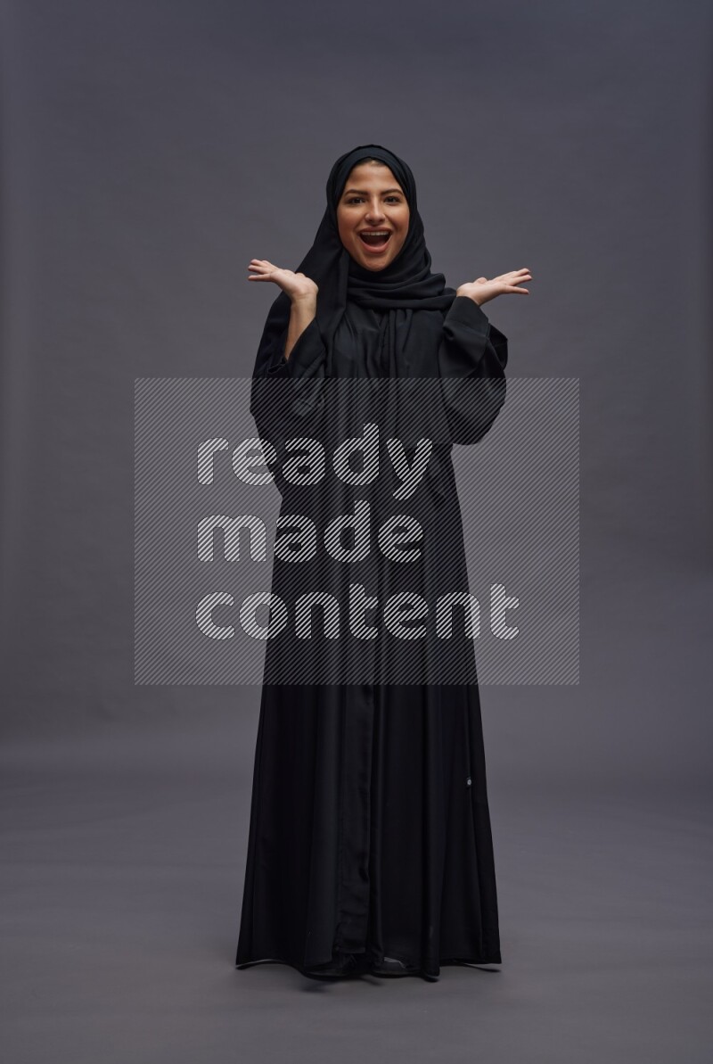 Saudi woman wearing Abaya standing hands behind head on gray background