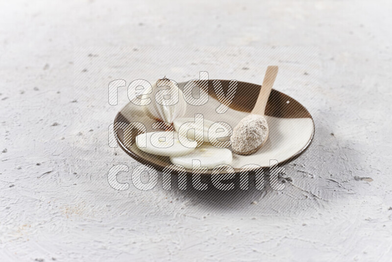 A wooden spoon full of onion powder with sliced onions, all on a pottery plate on white background