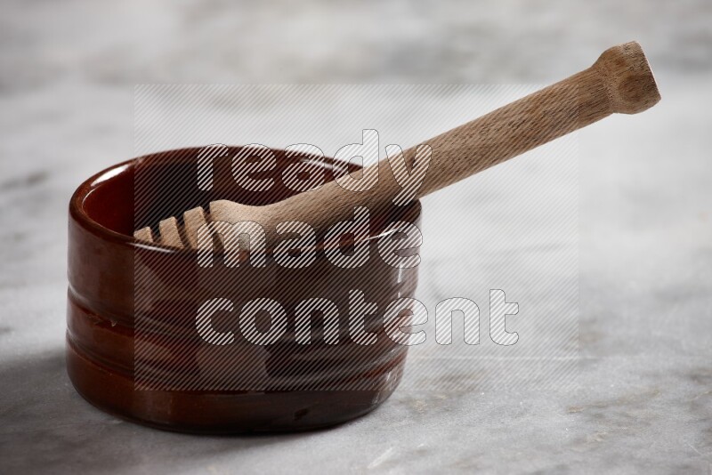 Brown pottery bowl with wooden honey dipper in it on grey marble background