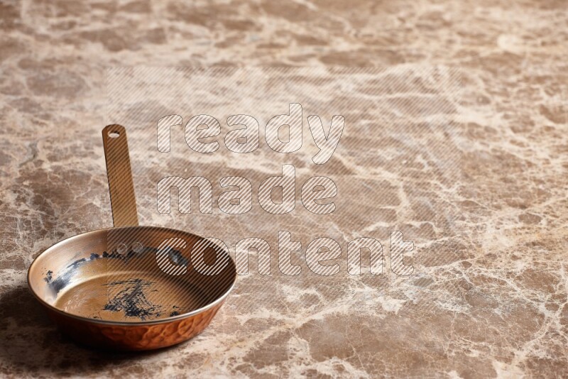 A small copper pan on beige marble background