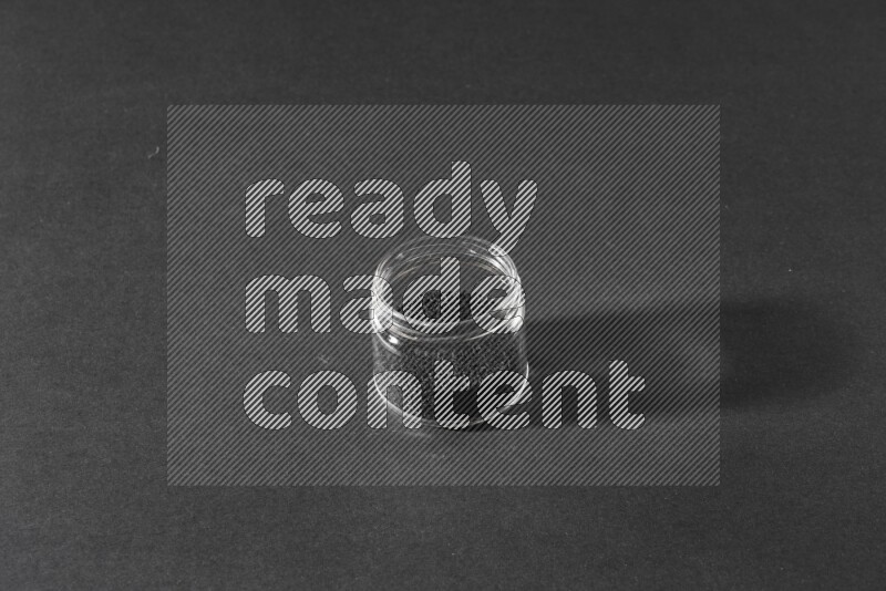 A glass jar full of black seeds on a black flooring